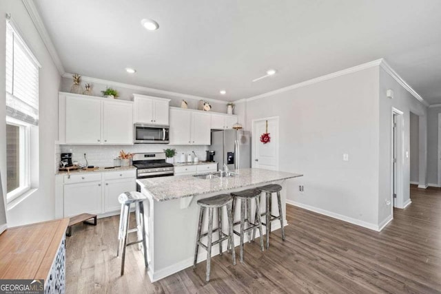6713 Moondancer Ct, Flowery Branch, GA 30542 - kitchen featuring stainless steel appliances, a center island with sink, ornamental molding, white cabinetry, and a kitchen breakfast bar
