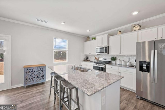 6713 Moondancer Ct, Flowery Branch, GA 30542 - kitchen featuring appliances with stainless steel finishes, ornamental molding, a center island with sink, a kitchen breakfast bar, and wood finished floors