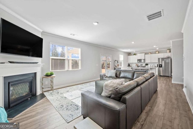 6713 Moondancer Ct, Flowery Branch, GA 30542 - living area featuring crown molding, healthy amount of natural light, light wood-type flooring, recessed lighting, and a glass covered fireplace