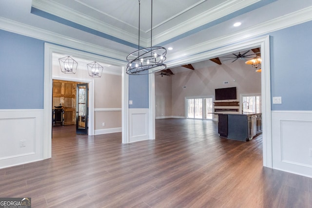unfurnished dining area featuring ornamental molding, dark wood finished floors, a decorative wall, wainscoting, and a tray ceiling