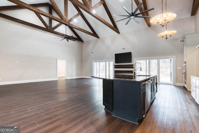 kitchen with open floor plan, pendant lighting, dark wood finished floors, ceiling fan with notable chandelier, and an island with sink