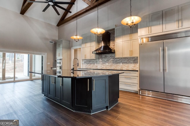 kitchen featuring a sink, wall chimney exhaust hood, appliances with stainless steel finishes, pendant lighting, and an island with sink