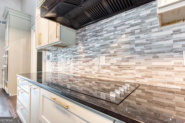 kitchen featuring wall chimney range hood, visible vents, dark wood finished floors, dark stone counters, and backsplash