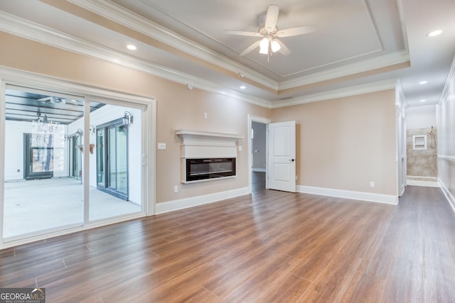 unfurnished living room featuring a ceiling fan, a glass covered fireplace, a raised ceiling, and wood finished floors