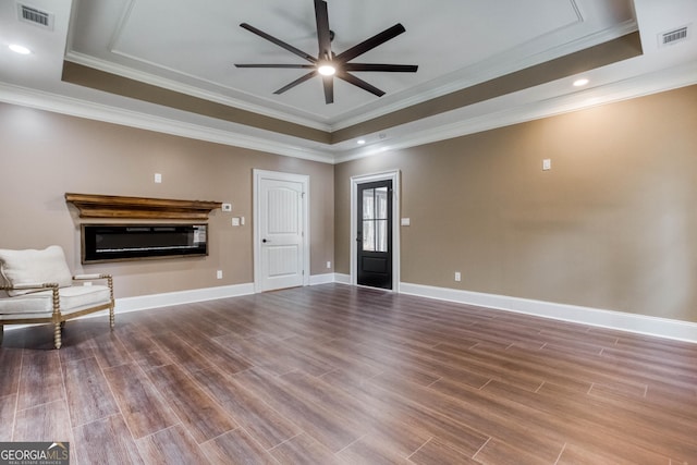 interior space with visible vents, a tray ceiling, wood finished floors, and a glass covered fireplace