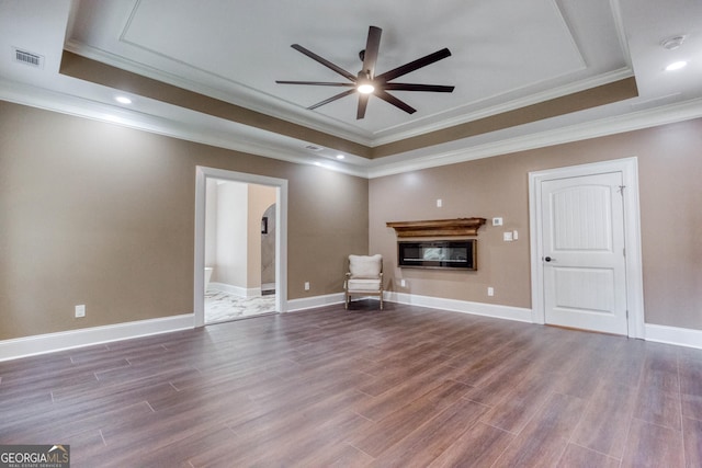 unfurnished room with a raised ceiling, visible vents, wood finished floors, and a glass covered fireplace