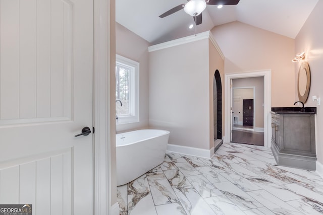 bathroom with baseboards, vaulted ceiling, marble finish floor, vanity, and a soaking tub