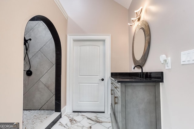 bathroom featuring marble finish floor, vanity, vaulted ceiling, and a tile shower