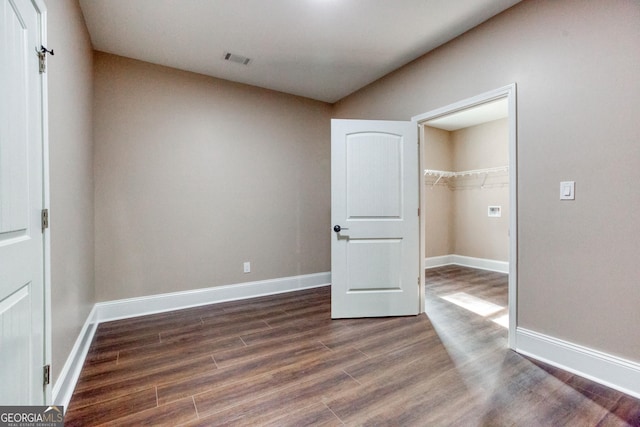 unfurnished bedroom with visible vents, a spacious closet, baseboards, dark wood finished floors, and a closet