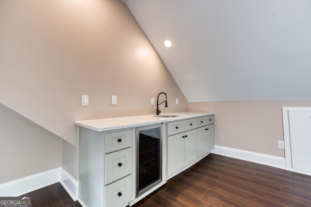 bar with a sink, beverage cooler, baseboards, dark wood-type flooring, and vaulted ceiling