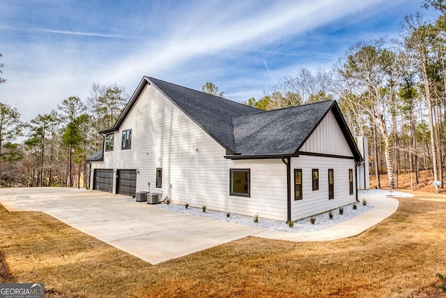 view of side of home with a lawn, driveway, roof with shingles, central AC unit, and an attached garage