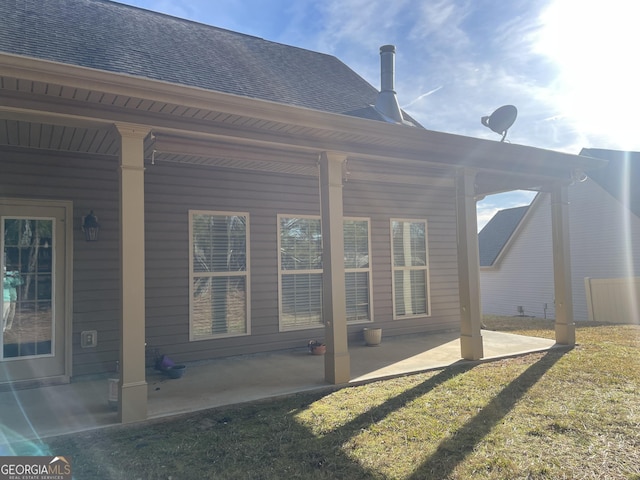 back of property featuring a lawn, roof with shingles, and a patio area