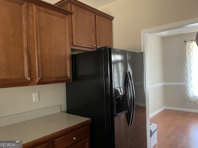 kitchen with light countertops, brown cabinets, light wood-style floors, and black fridge with ice dispenser