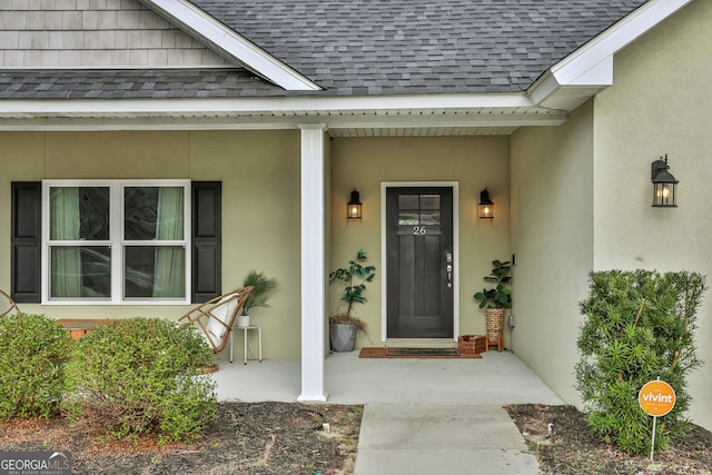 view of exterior entry featuring roof with shingles and stucco siding