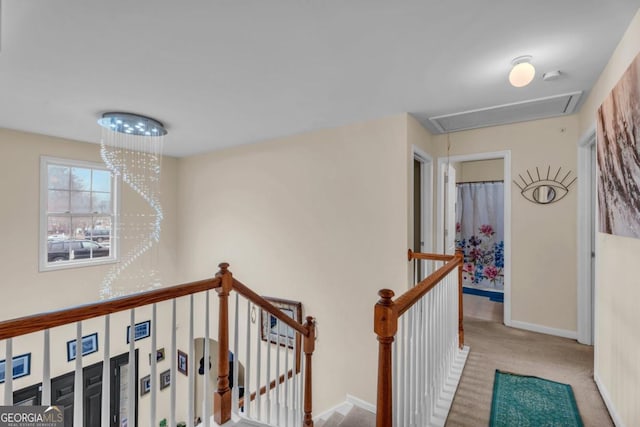 hallway with a chandelier, an upstairs landing, baseboards, carpet, and attic access