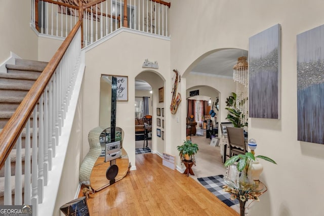 entrance foyer with arched walkways, wood finished floors, a high ceiling, stairs, and crown molding