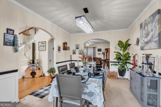 dining space with light wood-type flooring, arched walkways, crown molding, and ceiling fan with notable chandelier