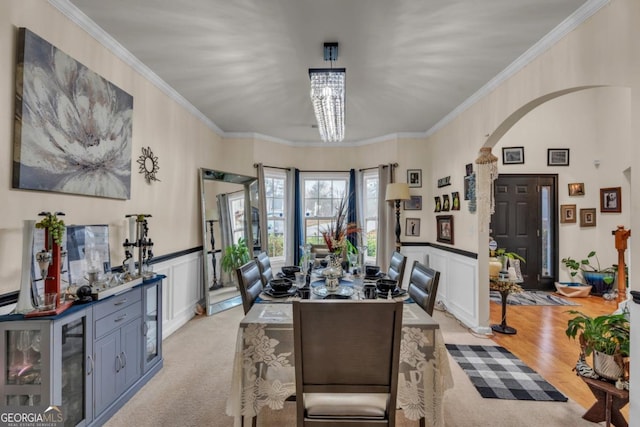 dining area with arched walkways, wainscoting, crown molding, and a decorative wall