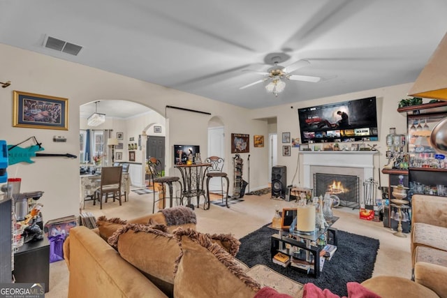 living area featuring arched walkways, a lit fireplace, light carpet, and visible vents