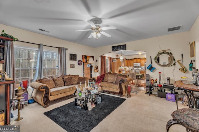 living area featuring arched walkways, visible vents, ceiling fan, and carpet flooring