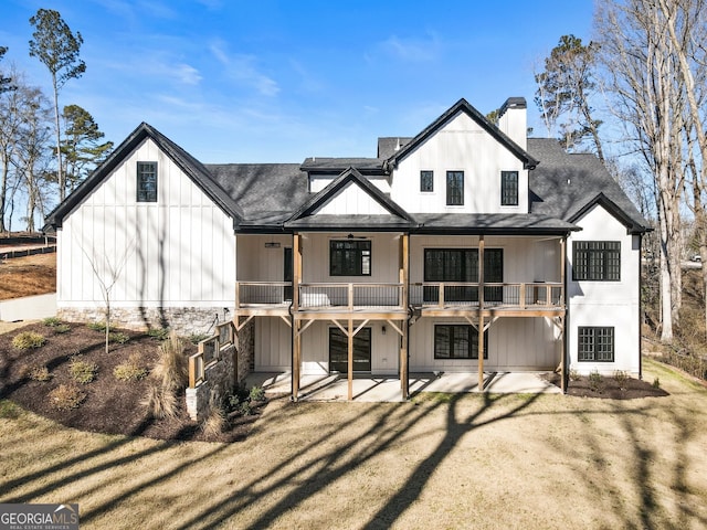 rear view of house with a shingled roof, a patio, a ceiling fan, a lawn, and a chimney