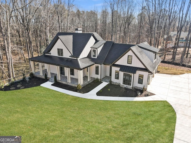 modern inspired farmhouse with a standing seam roof, metal roof, a porch, a chimney, and a front yard