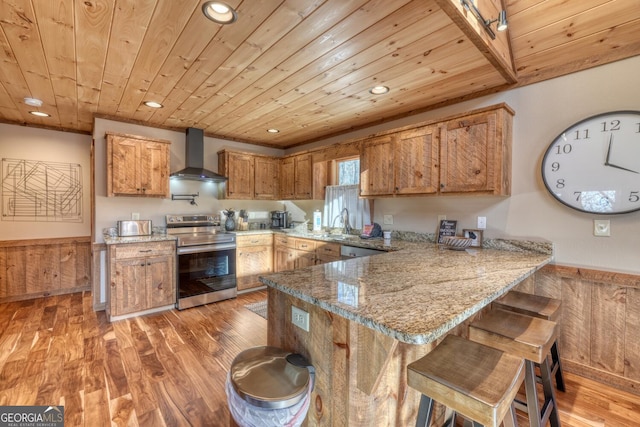 kitchen featuring a peninsula, wooden ceiling, wall chimney exhaust hood, and appliances with stainless steel finishes