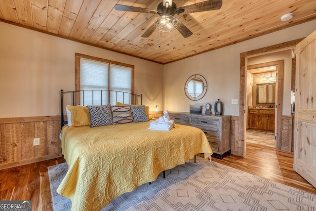 bedroom featuring a ceiling fan, a wainscoted wall, wood ceiling, ornamental molding, and light wood-type flooring