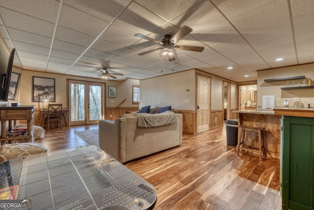 living area featuring a wainscoted wall, a drop ceiling, wood finished floors, and french doors