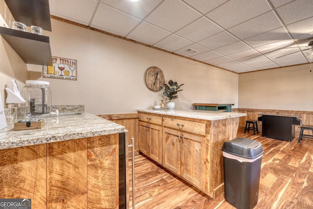 kitchen with brown cabinets, a peninsula, light stone countertops, a paneled ceiling, and light wood-style floors