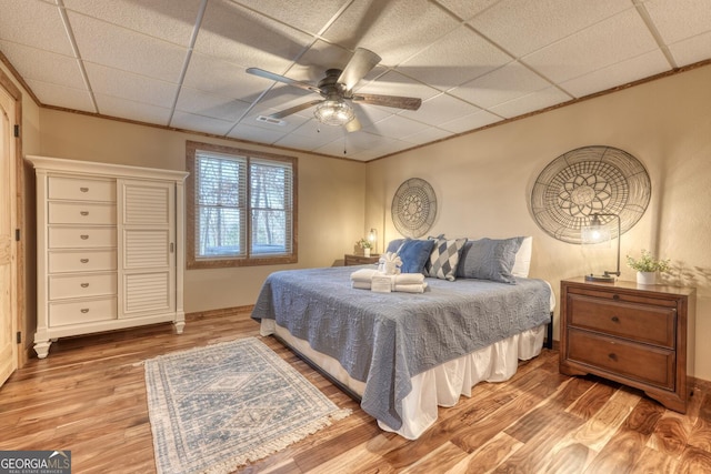 bedroom with ornamental molding, wood finished floors, and a paneled ceiling