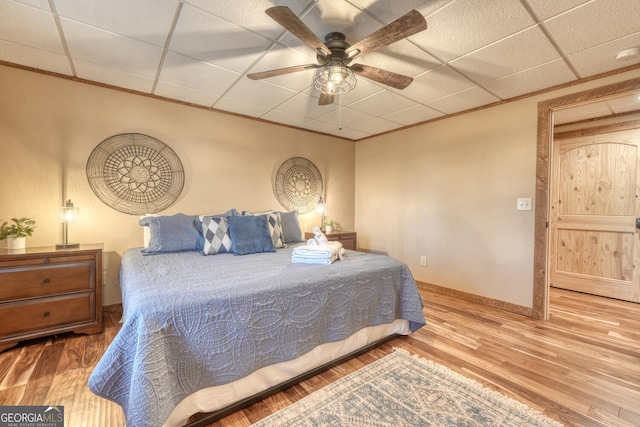 bedroom featuring baseboards, ceiling fan, ornamental molding, wood finished floors, and a paneled ceiling