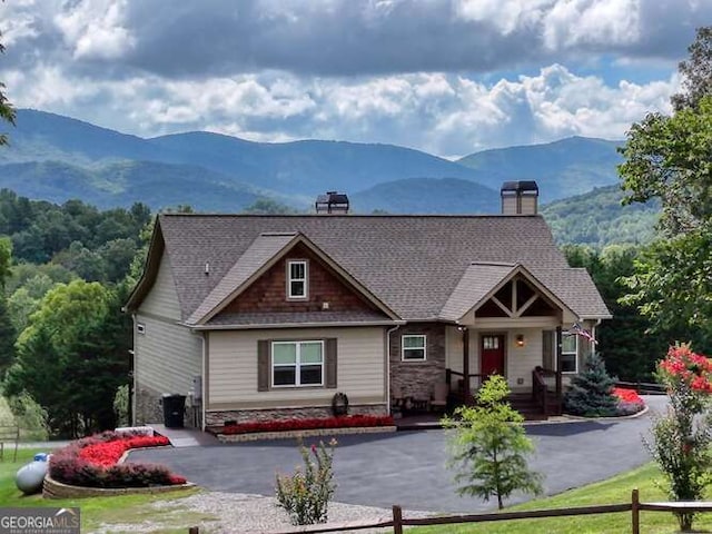 craftsman house featuring aphalt driveway, a mountain view, stone siding, roof with shingles, and a chimney