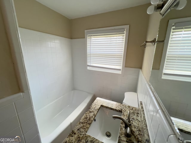 full bath with a wainscoted wall, vanity, tile walls, a tub, and toilet