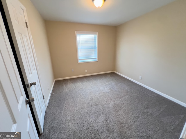 unfurnished room with baseboards and dark colored carpet