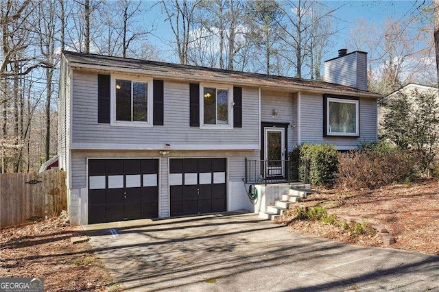 raised ranch featuring fence, an attached garage, driveway, and a chimney