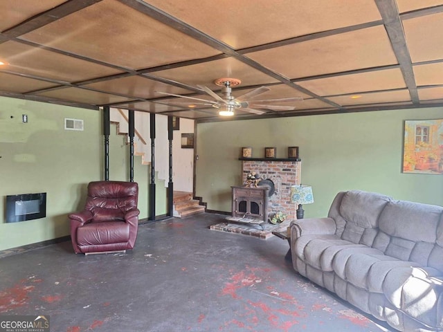 living room with visible vents, a ceiling fan, a wood stove, stairs, and concrete flooring