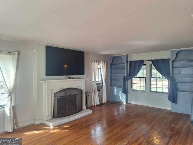 unfurnished living room featuring a brick fireplace, baseboards, and wood finished floors