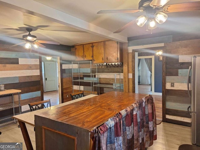 kitchen featuring light wood finished floors, wooden walls, a ceiling fan, and freestanding refrigerator