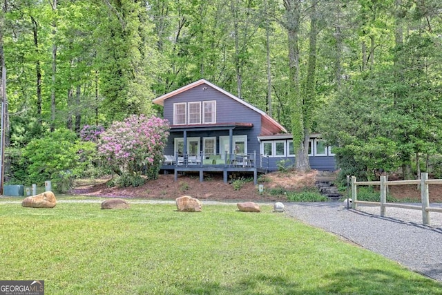 view of front of home with driveway, a front lawn, fence, and a view of trees