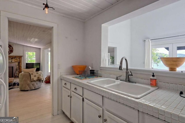 kitchen with tile countertops, white cabinetry, a sink, light wood-type flooring, and wooden ceiling