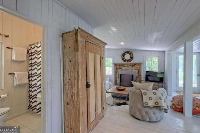 living area with a stone fireplace, wood ceiling, and light wood-style floors