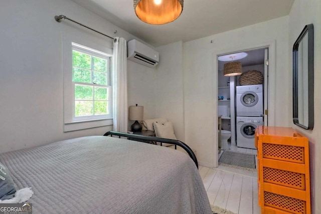 bedroom featuring stacked washer and clothes dryer, a wall mounted air conditioner, ensuite bath, and wood finished floors