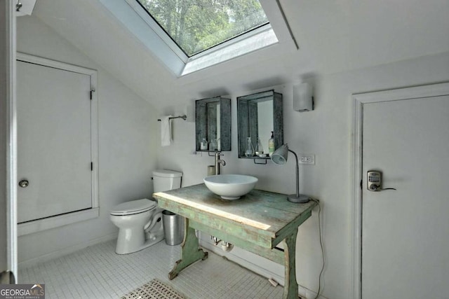 bathroom featuring vaulted ceiling with skylight, a sink, toilet, and tile patterned floors