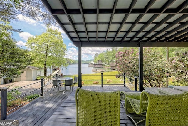 wooden terrace with a water view, a storage unit, an outbuilding, and outdoor dining space