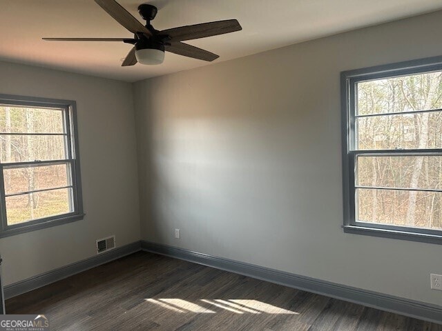 spare room featuring a ceiling fan, visible vents, dark wood finished floors, and baseboards