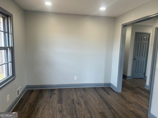 spare room with a healthy amount of sunlight, dark wood-style floors, baseboards, and visible vents