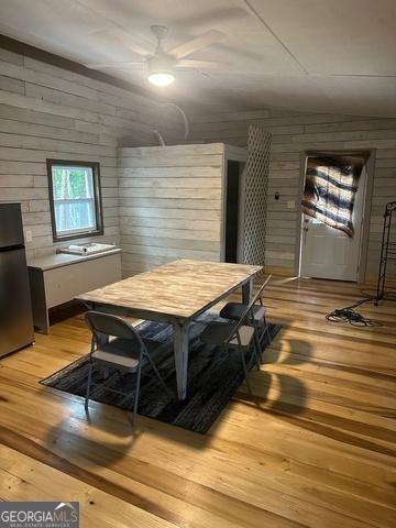 dining room featuring a ceiling fan, wood walls, and wood finished floors