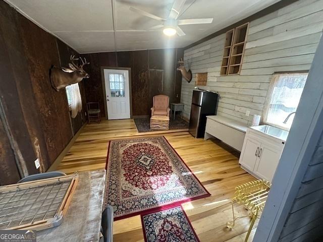 interior space with wooden walls, white cabinets, light wood-style flooring, freestanding refrigerator, and a sink