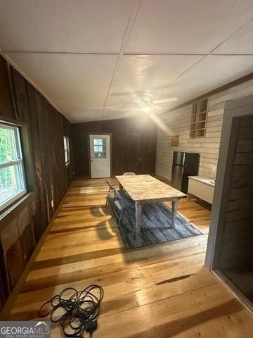 bedroom with lofted ceiling, light wood-style floors, wooden walls, and multiple windows